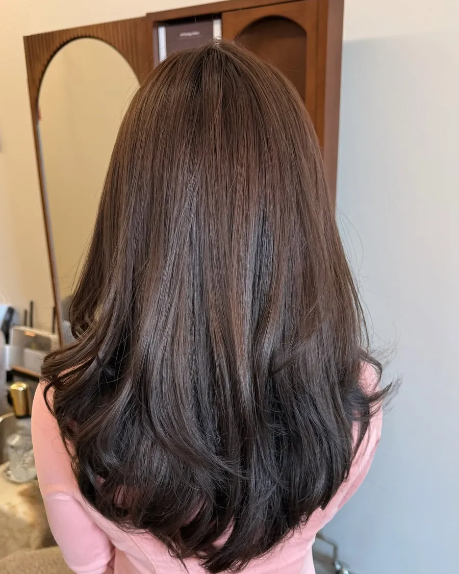 Back view of long chocolate-brown hair in front of the salon's arched walnut mirrors